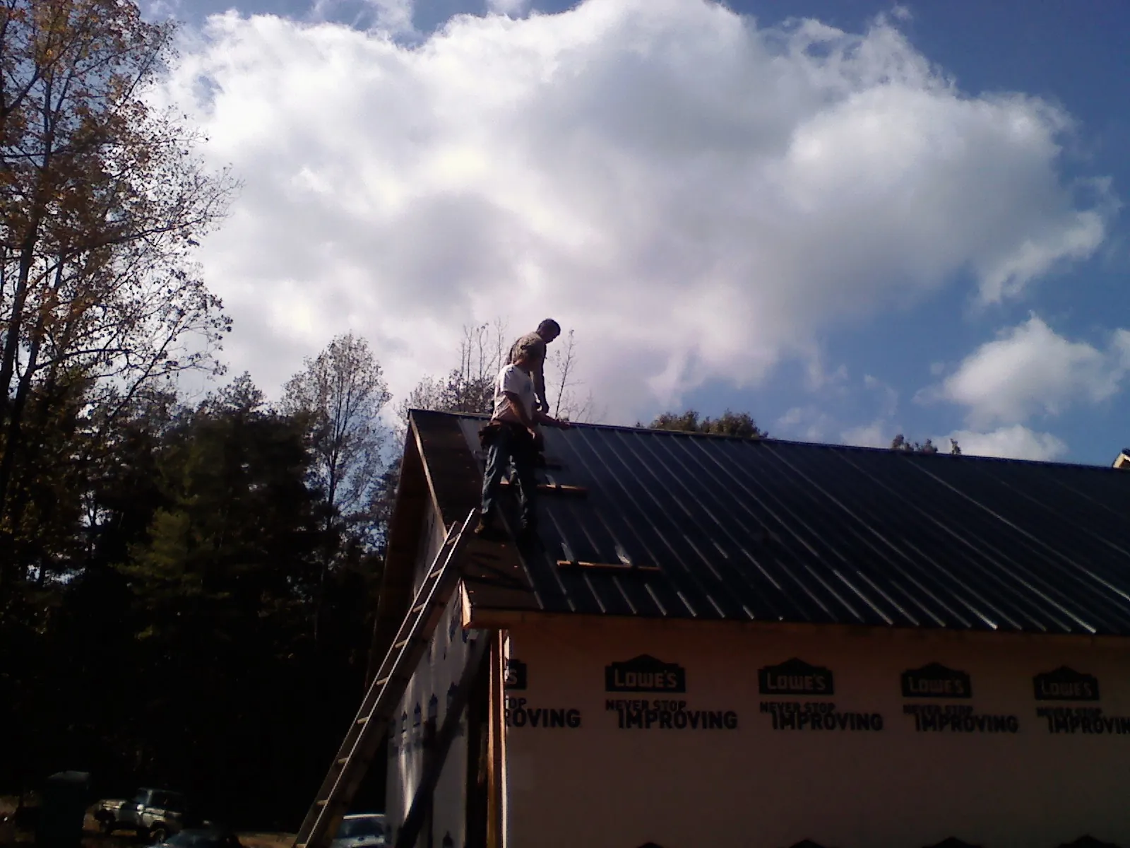 Roofer fastening dark metal panels high against a cloudy sky, from a Roof Inspection job in Waldwick
